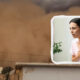 A woman in a pink shirt clutches her chest in distress, shown inside a white-framed cutout over a dusty, stormy city backdrop, suggesting chest pain or a heart emergency.