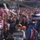 Large stadium crowd cheering and waving signs that read GOOOOOOAL, celebrating a goal with people of various ages and outfits