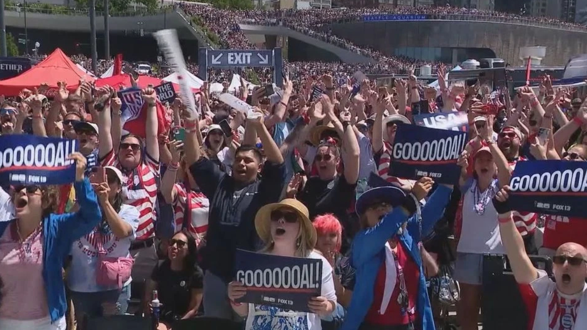 Large stadium crowd cheering and waving signs that read GOOOOOOAL, celebrating a goal with people of various ages and outfits