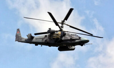 Russian military attack helicopter in flight, side-mounted missiles visible against a blue sky.