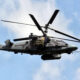 Russian military attack helicopter in flight, side-mounted missiles visible against a blue sky.