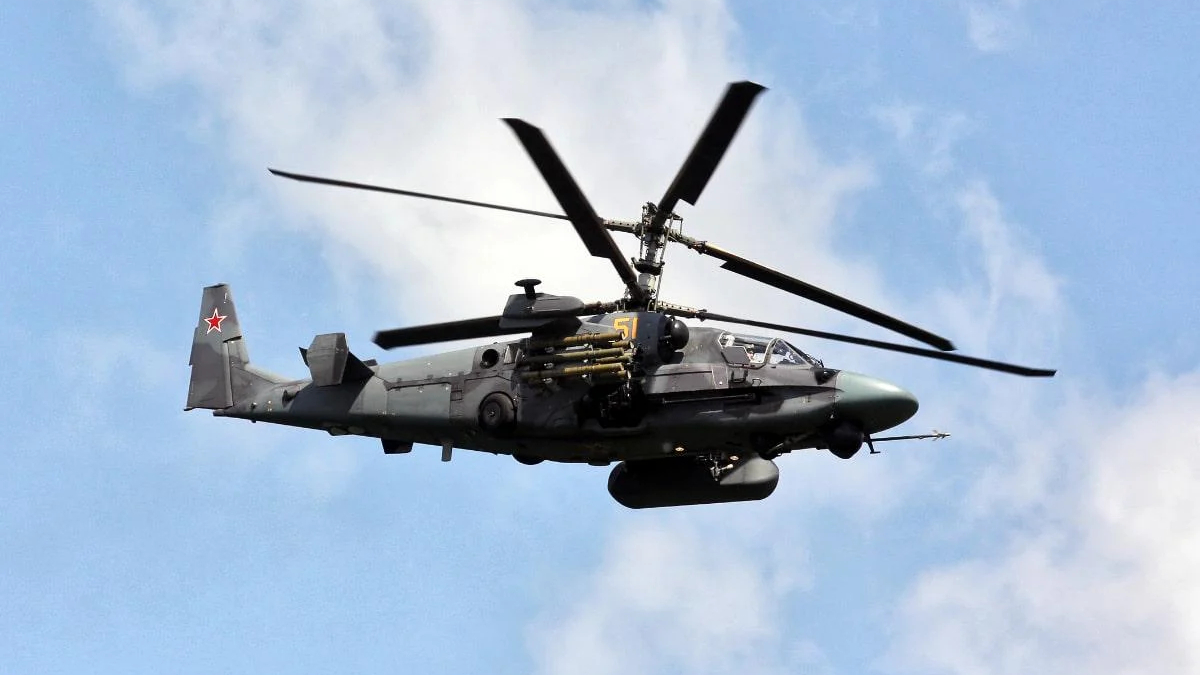 Russian military attack helicopter in flight, side-mounted missiles visible against a blue sky.