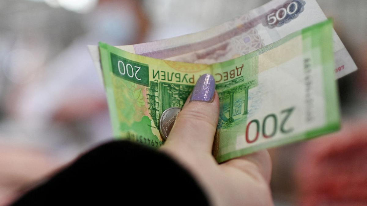 Hand with purple nail polish holding green 200 currency notes, a 500 note visible in the background, focusing on cash.