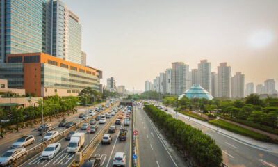 Busy urban highway lined with modern skyscrapers and a glass pyramid building at sunset, with heavy traffic on both sides.
