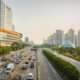 Busy urban highway lined with modern skyscrapers and a glass pyramid building at sunset, with heavy traffic on both sides.