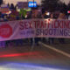 Group of protesters marching at night, carrying a large banner that says 'Sex Trafficking, No More Shootings' with a red stop sign on the left.