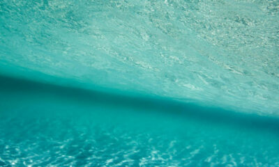 Aerial view of turquoise ocean water with sunlight ripples and a dark diagonal shadow across the surface