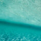 Aerial view of turquoise ocean water with sunlight ripples and a dark diagonal shadow across the surface