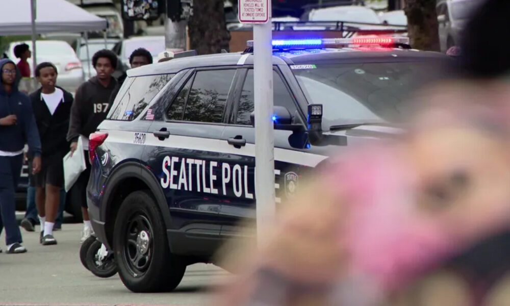 Seattle Police SUV with blue and red lights at a street event, with bystanders in the background.