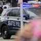 Seattle Police SUV with blue and red lights at a street event, with bystanders in the background.