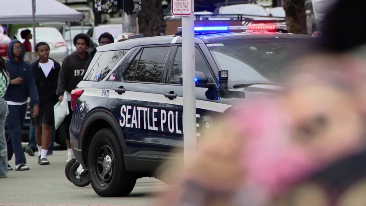 Seattle Police SUV with blue and red lights at a street event, with bystanders in the background.
