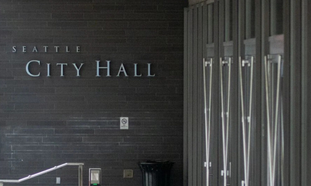 Exterior view of Seattle City Hall with a dark brick wall and large metal lettering reading 'City Hall' at the entrance