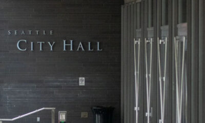 Exterior view of Seattle City Hall with a dark brick wall and large metal lettering reading 'City Hall' at the entrance