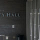 Exterior view of Seattle City Hall with a dark brick wall and large metal lettering reading 'City Hall' at the entrance