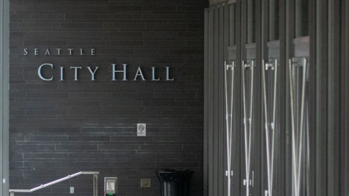Exterior view of Seattle City Hall with a dark brick wall and large metal lettering reading 'City Hall' at the entrance