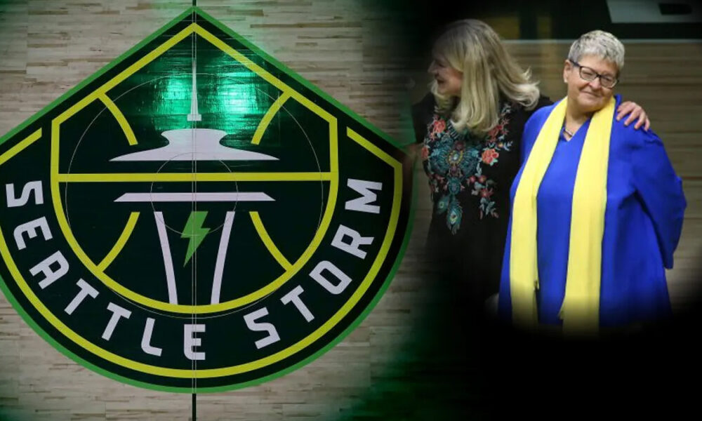 Seattle Storm emblem fills the left side as two women walk together on the right, one in a blue gown with a yellow scarf, smiling.