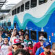 Crowded train platform with a blue and teal wave-patterned double-decker train and passengers boarding. Crowded train platform with a blue and teal wave-patterned double-decker train and passengers boarding.