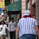 Busy city sidewalk with pedestrians and storefronts, red lantern decorations overhead.