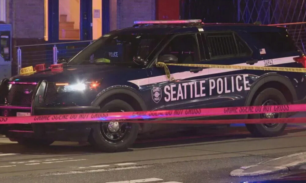 Seattle Police SUV at night with crime scene tape crossing the street and flashing lights nearby.