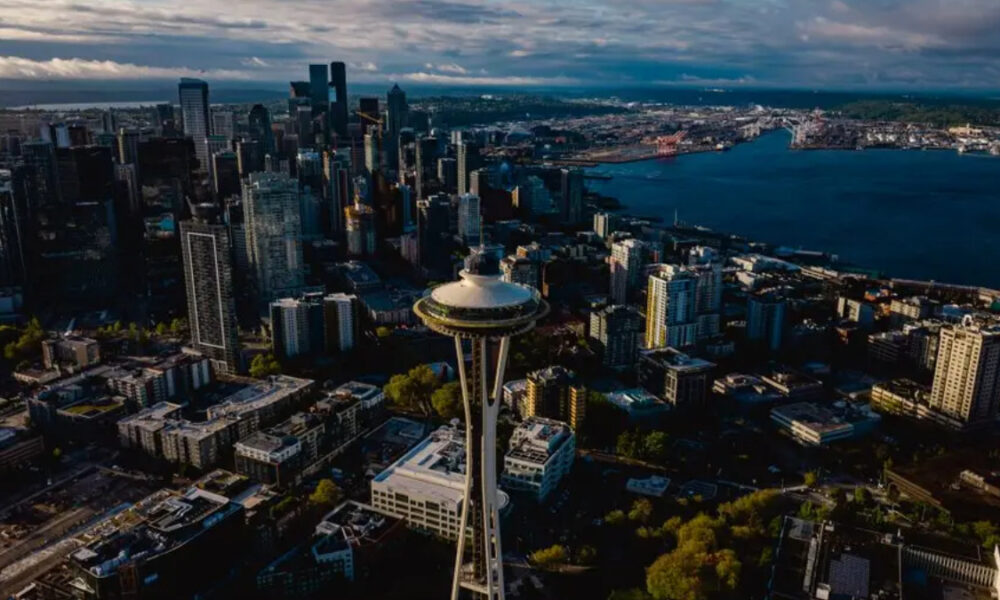 Aerial view of downtown Seattle with the Space Needle rising among skyscrapers and Puget Sound beyond.