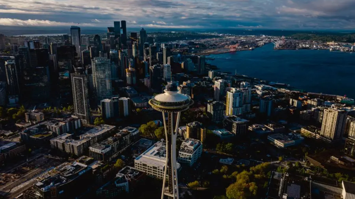 Aerial view of downtown Seattle with the Space Needle rising among skyscrapers and Puget Sound beyond.
