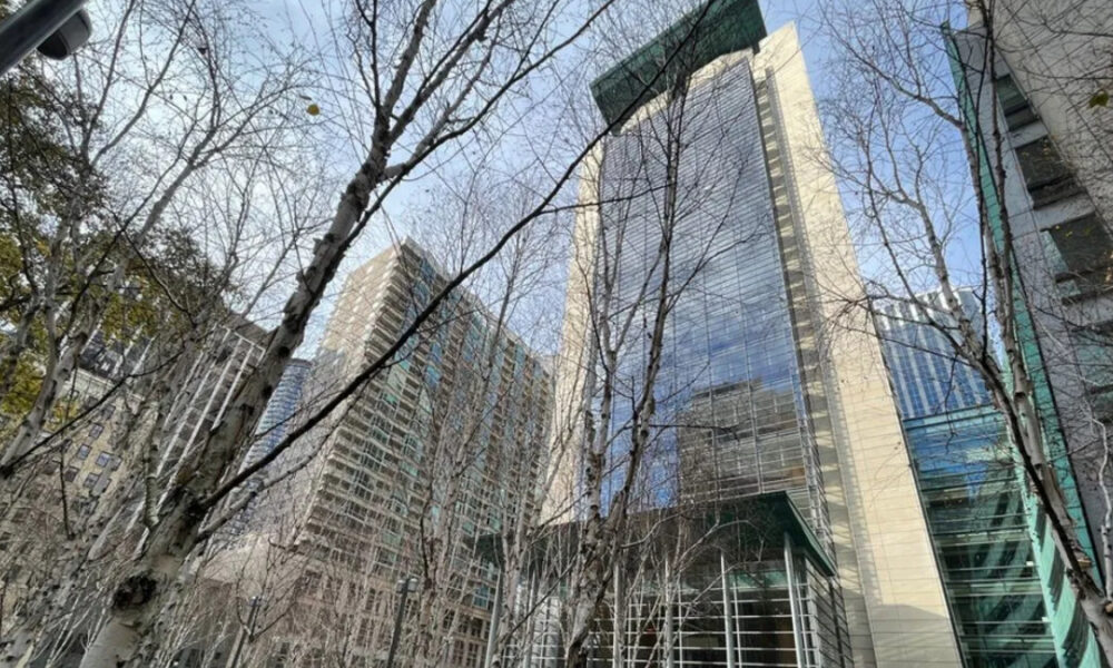 Tall glass skyscrapers rise behind bare winter trees in an urban plaza.