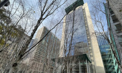 Tall glass skyscrapers rise behind bare winter trees in an urban plaza.