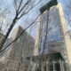 Tall glass skyscrapers rise behind bare winter trees in an urban plaza.