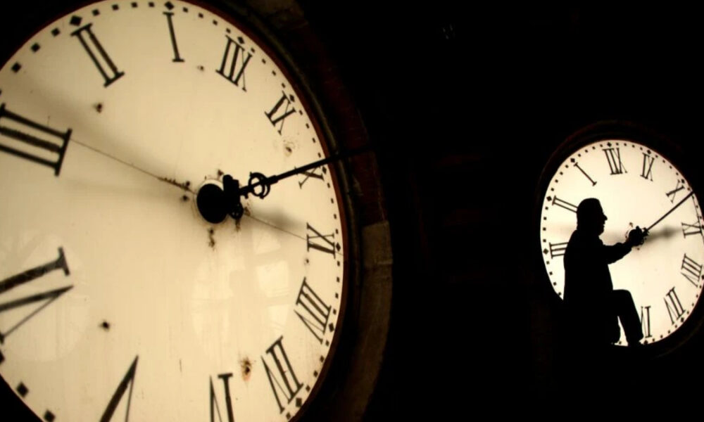 Silhouette of a person climbing inside a large clock face with Roman numerals at night.