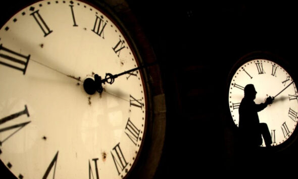 Silhouette of a person climbing inside a large clock face with Roman numerals at night.