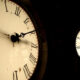 Silhouette of a person climbing inside a large clock face with Roman numerals at night.