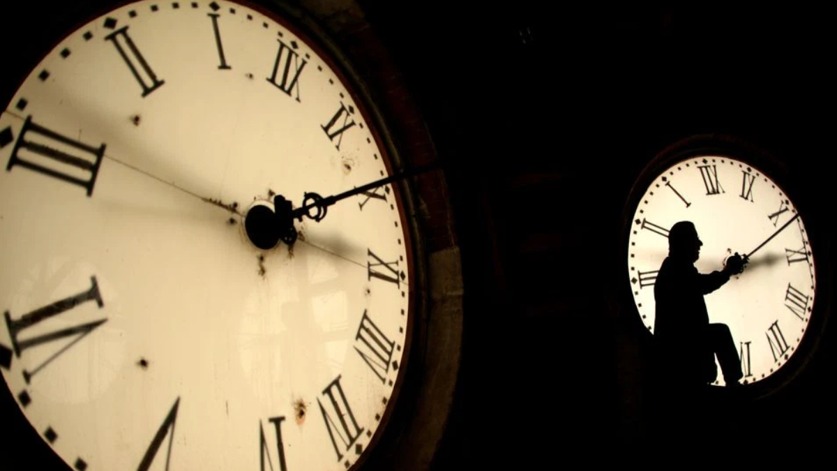 Silhouette of a person climbing inside a large clock face with Roman numerals at night.