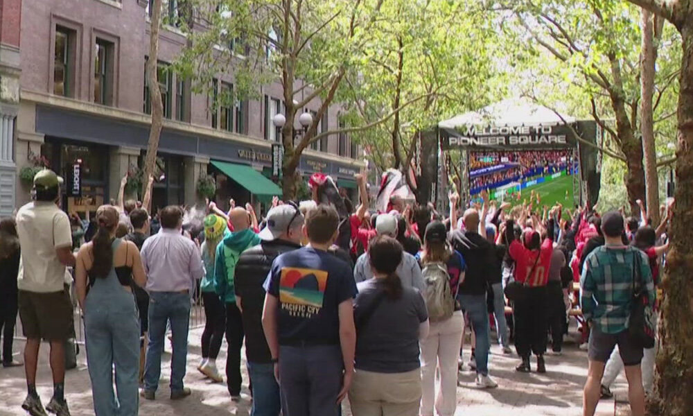 Crowd of people in an urban plaza watching a large outdoor screen that says Welcome to Pioneer Square.