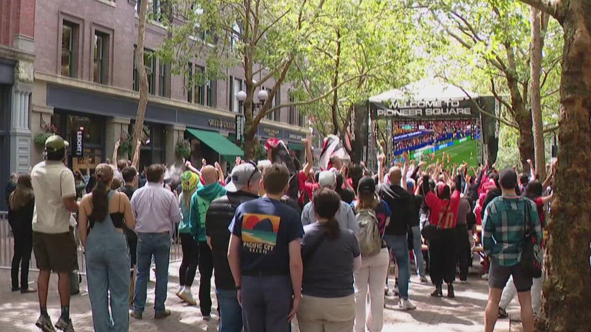 Crowd of people in an urban plaza watching a large outdoor screen that says Welcome to Pioneer Square.