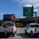 Emergency response vehicles block a highway under an overpass; a digital left-arrow sign and orange cones indicate a incident scene.