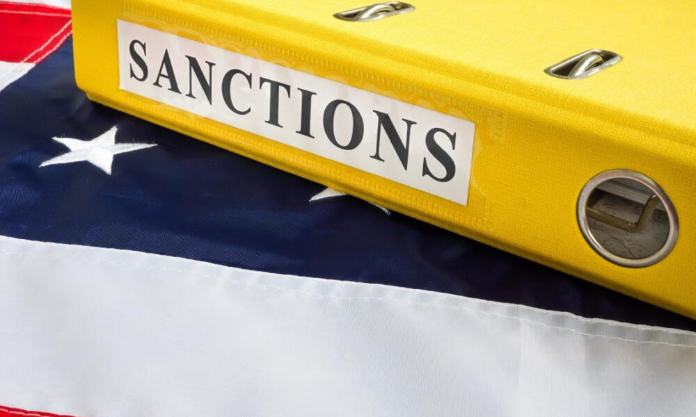 Close-up of a bright yellow binder labeled 'SANCTIONS' resting on a folded American flag.