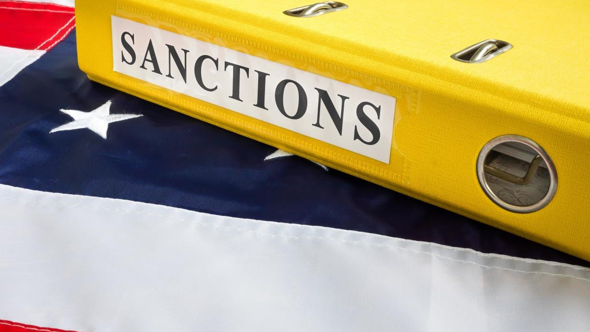 Close-up of a bright yellow binder labeled 'SANCTIONS' resting on a folded American flag.