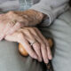 Close-up of an elderly person’s hands folded over a wooden cane, wearing rings, conveying aging and care.