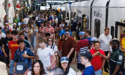 Crowded train platform with many passengers waiting and boarding a silver commuter train nearby edge doors open.