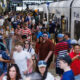 Crowded train platform with many passengers waiting and boarding a silver commuter train nearby edge doors open.