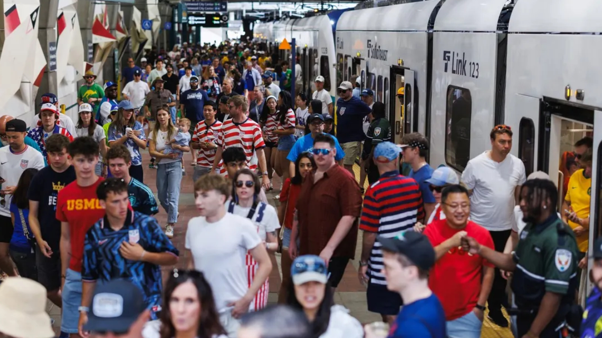 Crowded train platform with many passengers waiting and boarding a silver commuter train nearby edge doors open.