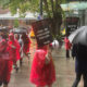 Group of protesters in red ponchos marching on a rainy city sidewalk, holding signs that say 'On Strike' and 'One Job Should Be Enough'.