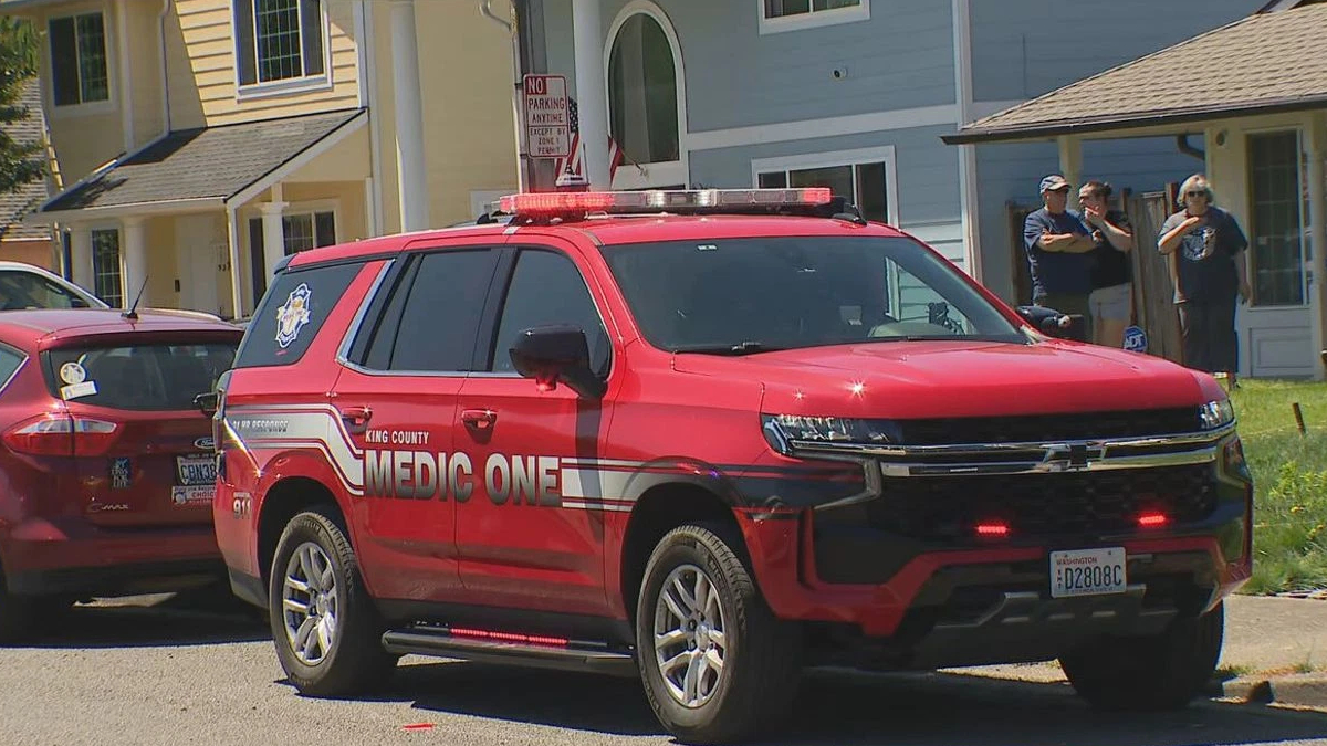 Red King County Medic One SUV parked on a residential street with flashing lights on top and people standing near a blue house in the background