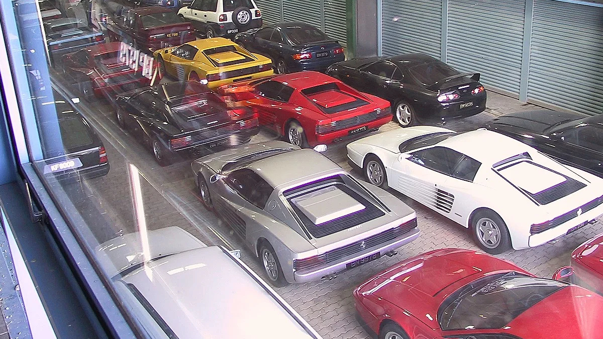Overhead view of a showroom filled with colorful sports cars parked in rows inside a glass-walled space