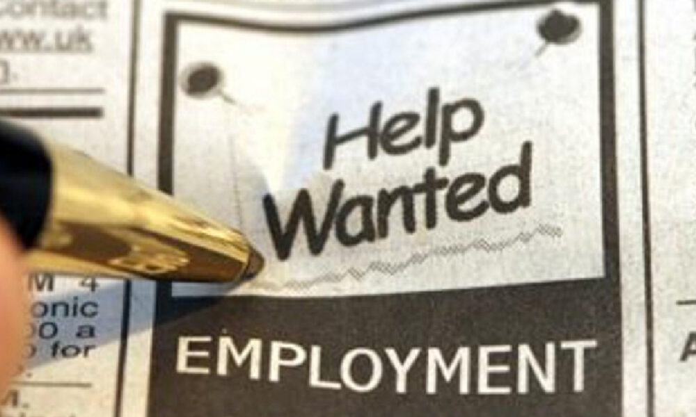 Close-up of a newspaper ad with 'Help Wanted' and 'EMPLOYMENT' visible, a gold pen pointing at it.