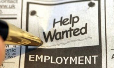 Close-up of a newspaper ad with 'Help Wanted' and 'EMPLOYMENT' visible, a gold pen pointing at it.