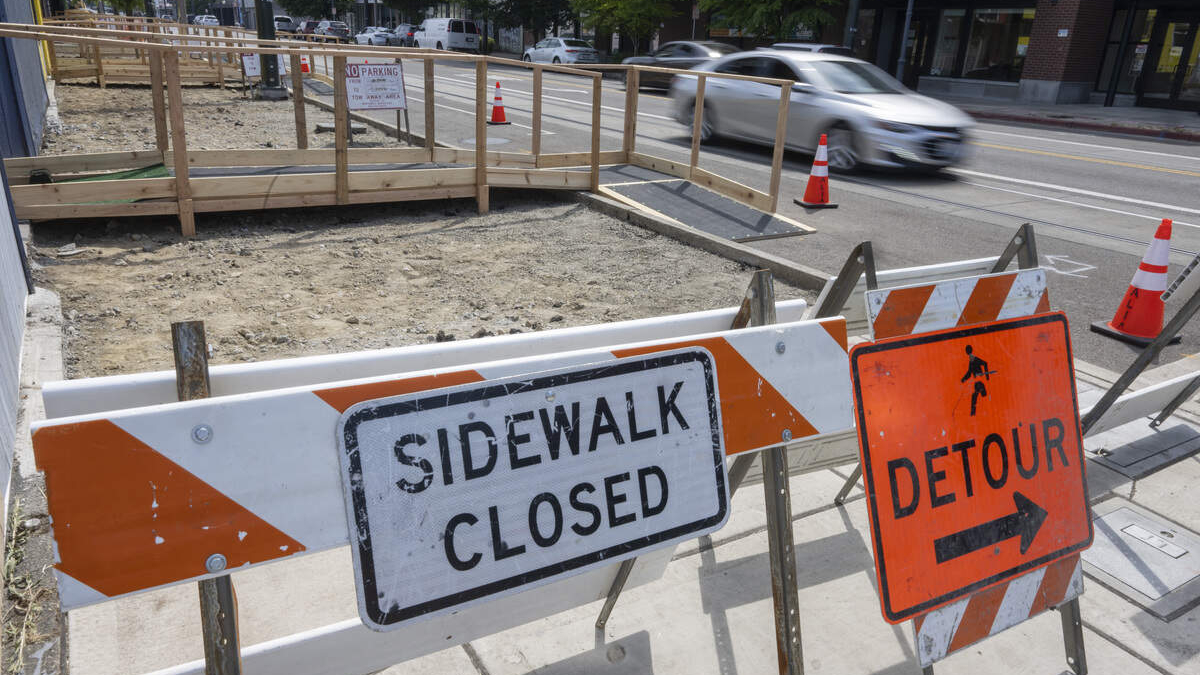 Construction site blocks the sidewalk; signs read 'Sidewalk Closed' and 'Detour' with orange cones nearby.