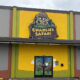 Bright yellow storefront with a large Charlie's Safari sign above the entrance and a double glass door featuring jungle cartoon characters outside a green and yellow facade