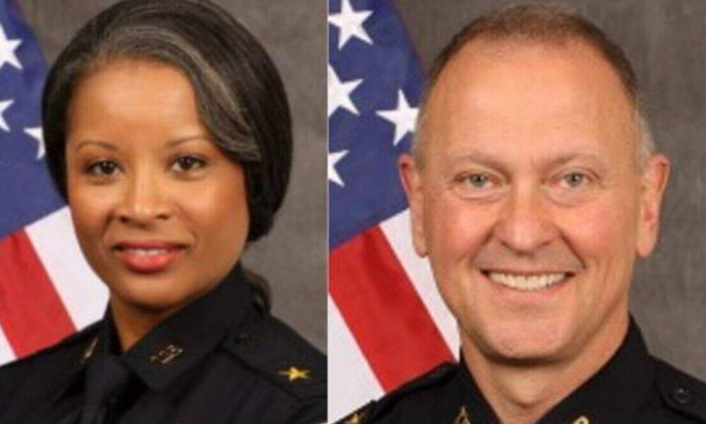 Two police officers, a woman (left) and a man (right), in formal uniform with an American flag backdrop.