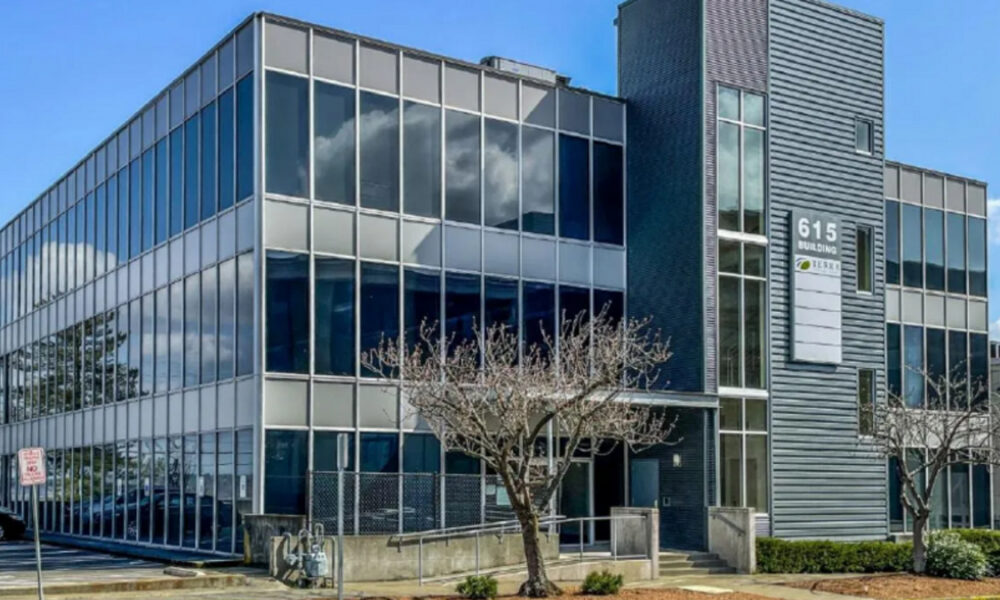 Modern glass office building with reflective windows and a tall vertical facade labeled '615 Building' against a blue sky.